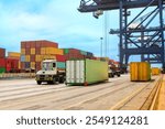 A massive container crane at the Port of San Antonio, Chile, lifts and moves the colorful stacked containers as trucks line up for transport.