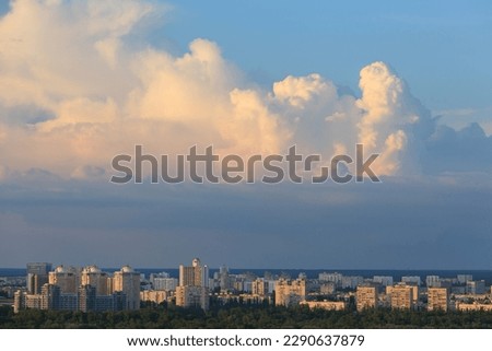 Massive cumulus clouds hang above the city, illuminated by the setting sun.