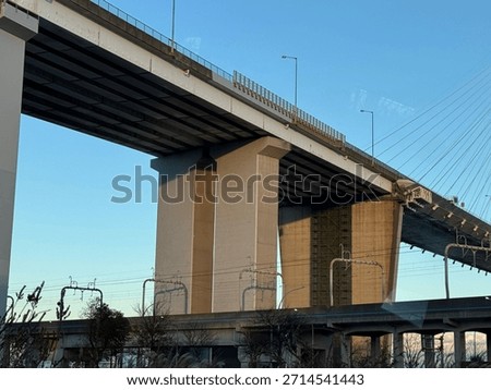 A massive elevated roadway structure dominates the frame, supported by thick, imposing concrete piers