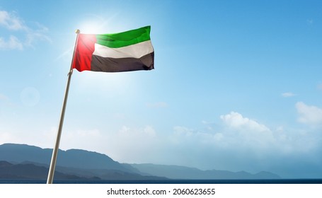 Massive flag of UAE flying against panoramic mountain range and sky. United Arab Emirates National Day is celebrated on 2nd December.