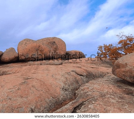 Massive granite boulders sit atop a weathered rocky plateau under a vibrant sky, with autumn foliage peeking in—capturing the raw beauty of nature’s stonework.