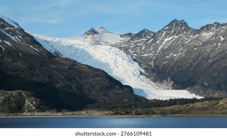 A massive ice river cascading down a steep mountain valley toward a calm body of water