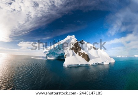 A massive iceberg, sculpted from a glacial landscape, floats in a cold, blue ocean under a clear Arctic sky, symbolizing the effects of climate change.