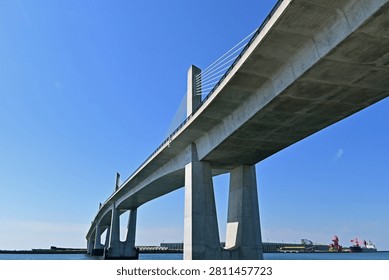 Massive low angle view of a modern concrete cable stayed bridge with cargo ships in a harbor under a clear blue sky, Fukushima Japan.