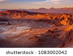 A massive moon crater with salt deposit in the middle of eerie terrain at the Valle de Luna, or Moon Valley, at San Pedro de Atacama. Sunset light casts shadow on mountains and changes its colours.