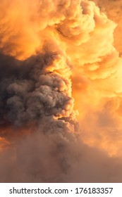 A massive plume of dark ash and smoke billows from the Tungurahua volcano into an orange-and-golden sunset sky in the Ecuadorian Andes, a dramatic display of natural power.