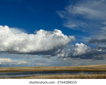 Massive prairie cloud formations drifting over open Alberta landscape with deep blue sky and expansive horizon creating cinematic big sky atmosphere