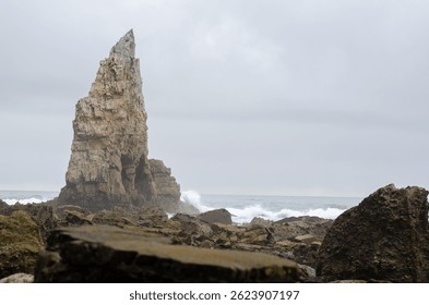 Massive sea stack rises above rocky shore with waves crashing against the cliffs on a moody, overcast day. Perfect for concepts of nature, adventure, and travel. - Powered by Shutterstock - Get 15% off with code: PIKWIZARD15