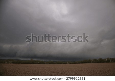 Massive shelf cloud formation approaching over plowed agricultural fields, severe thunderstorm front and extreme weather background, dramatic dark sky, global warming and climate change risk concept for agriculture with copy space for text