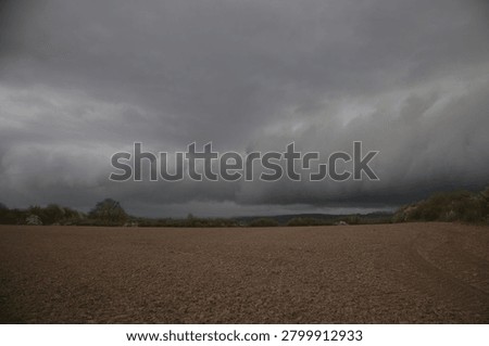 Massive shelf cloud formation approaching over plowed agricultural fields, severe thunderstorm front and extreme weather background, dramatic dark sky, global warming and climate change risk concept for agriculture with copy space for text