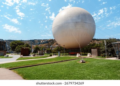 Massive spherical structure in park setting under blue sky on a sunny day in a vibrant urban area