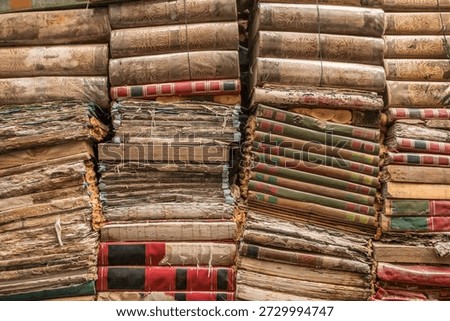 A massive stack of weathered antique books and manuscripts with leather bindings piled high inside the famous Libreria Acqua Alta bookstore in Venice.
