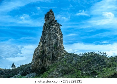 A massive stone tower formation stands majestically on a grassy hill with another rock in the distance.