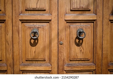 Massive wooden entrance doors with round handles and small keyhole close up. Double doors in solid wood in natural wooden color with large round iron knockers. Bi folding entrance doors in wood