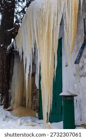 Massive yellowish icicles dramatically drape from a weathered garage roof, creating a stunning frozen spectacle. Winter's raw power transforms mundane structures into icy wonders