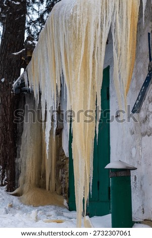 Massive yellowish icicles dramatically drape from a weathered garage roof, creating a stunning frozen spectacle. Winter's raw power transforms mundane structures into icy wonders
