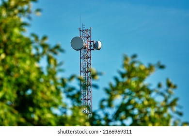 Mastre con antenas de teléfono celular contra el cielo azul. Árbol con hojas verdes.