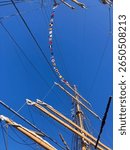 Mast, yards, furled sails, and signal flags of a traditionally rigged barque beneath a deep blue sky