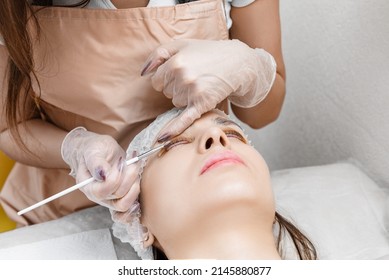 Master Applies Care Perm Cream To Eyelashes. Eyelash Care Treatment: Eyelash Lifting, Lash Lamination. Close-up Face During Lash Lift Laminating Procedure. Young Model With Brunette Hair.