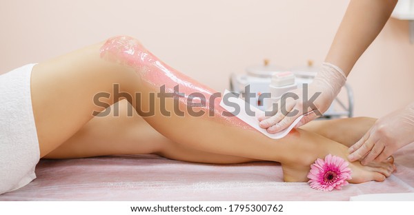 A master applies pink depilatory wax to\
a young woman\'s leg for hair removal. Depilation with wax. Beauty\
concept. Place for text. Selective\
focus.