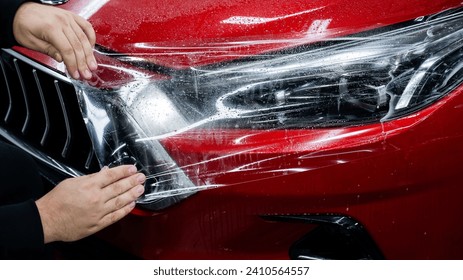 The master applies vinyl film to the headlight of a red car.  - Powered by Shutterstock