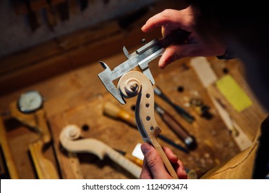 Master artisan luthier working on creation of a violin scroll. detailed work on wood with tools. Men's hands Measures the thickness of the scroll with meter . on the background of a workshop