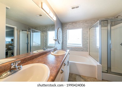 Master Bathroom With A Warm Lightning And Stone Tile Walls. There Is A Double Vanity Sink With Granite Top Near The Drop In Tub Against The Window Beside The Shower Stall With Glass Enclosure.