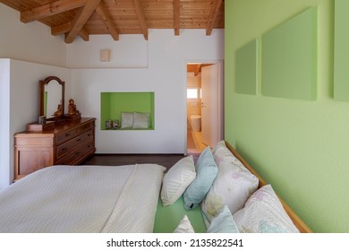 Master bedroom with large bed, nightstand, green walls and exposed wooden beams. Nobody inside.