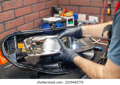 A Master In Black Gloves Installs A Bi-diode Lens In The Headlight Housing.Car Headlight During Repair And Cleaning.The Mechanic Restores The Headlight Of The Car. Restoration Of Automotive Optics.