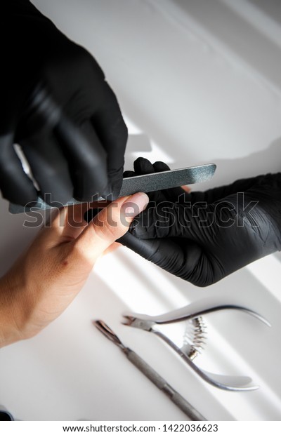 a master in black vinyl\
gloves gives a manicure to a white girl. shaping nails with a nail\
stick