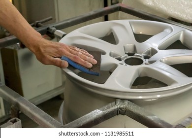 Master body repair man is working on preparing the surface of the aluminum wheel of the car for subsequent painting in the workshop, cleaning and leveling the wheel with the help of abrasive material
