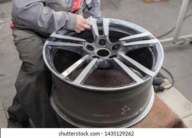 Master body repair man is working on preparing the surface of the aluminum wheel of the car for subsequent painting in the workshop, cleaning and leveling the disk with the help of abrasive material - Powered by Shutterstock