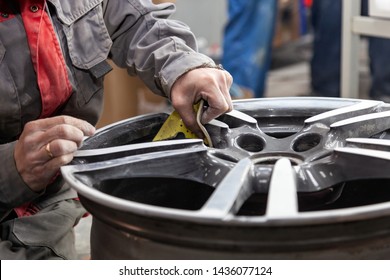 Master body repair man is working on preparing the surface of the aluminum wheel of the car for subsequent painting in the workshop, cleaning and leveling the disk with the help of abrasive material - Shutterstock ID 1436077124