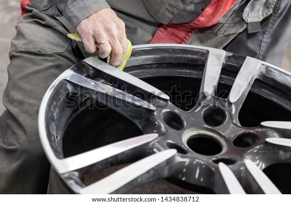 Master body repair man is working on preparing\
the surface of the aluminum wheel of the car for subsequent\
painting in the workshop, cleaning and leveling the disk with the\
help of abrasive\
material