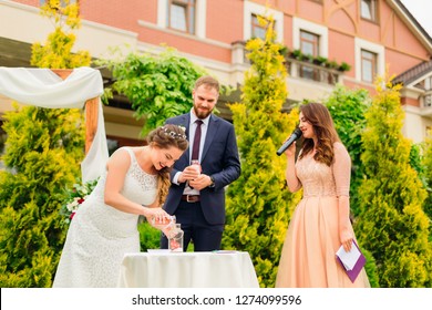 The Master Of Ceremonies Holds A Sand Ceremony And Newlyweds In Turn Pour In Unity Vase Sand Of Different Colors. Wedding Sand Ceremony