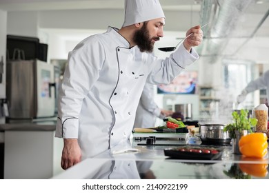 Master chef tasting gourmet dish while cooking food for dinner service at fine dining restaurant. Skilled cook checking meal taste after added fresh organic vegetables and ingredients in kitchen. - Powered by Shutterstock