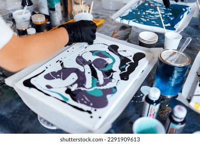 Master class on an Acrylic Fluid Pouring. Teacher and teen girl paint with liquid acrylic in an art workshop. Fluid Art. Dirty glass technique. There are paintings, paints and brushes on the table Art - Shutterstock ID 2291909613
