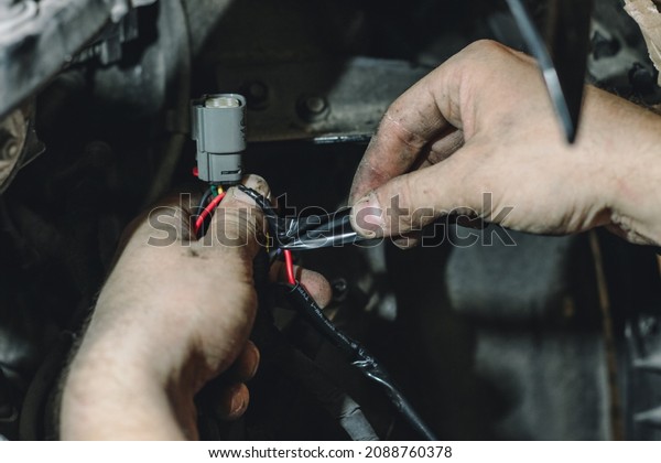 The master connects the wires under the hood of the\
car and insulates them. The concept of repairing the electrics of\
the car. An electrician is engaged in connecting the wires of the\
car.