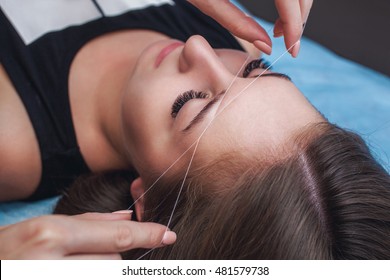 Master corrects makeup, gives shape and thread plucks eyebrows in a beauty salon. Professional care for face.