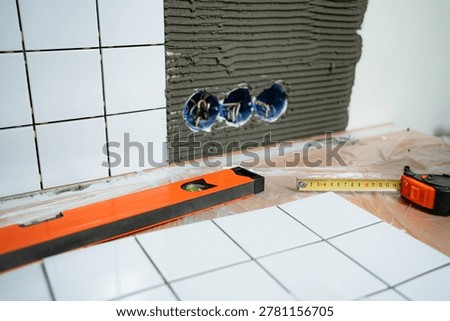 Master craftsman installing white ceramic kitchen tiles, applying adhesive mortar to the wall with a notched trowel, ensuring correct alignment with a spirit level during renovation work