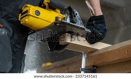 Master cuts the board with a circular saw in the workshop. Close-up of a carpenter's hands at work. 
