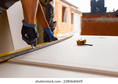 Master is cutting plasterboard using scalpel, cutter tool. Measuring tape for measurement placed on the gypsum board in workshop at the construction site. - Powered by Shutterstock