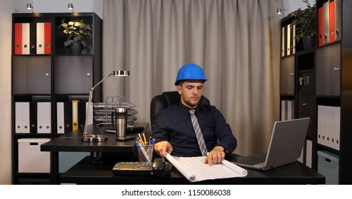 Master Engineer Working Using Computer Laptop Reading and Examining Blueprint Plans While Sitting in Corporate Office Room