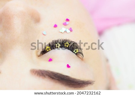 The master of eyelash extension decorates the girl's eyelashes with rhinestones, hearts and stars. Creative eyelash extensions, eye makeup.
