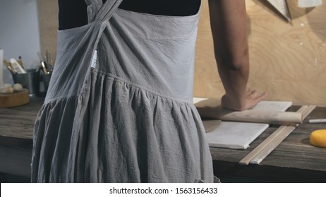 Master female potter wearing an apron preparing and rolling clay with a rollingpin. Female hands rolling out raw clay with wooden rolling pin - Powered by Shutterstock