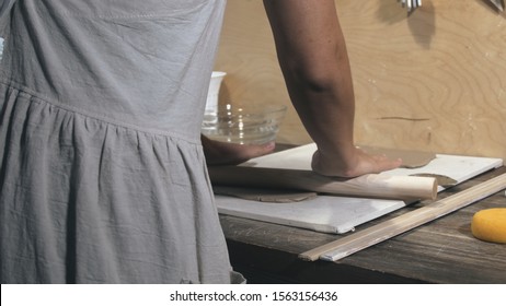 Master female potter wearing an apron preparing and rolling clay with a rollingpin. Female hands rolling out raw clay with wooden rolling pin - Powered by Shutterstock