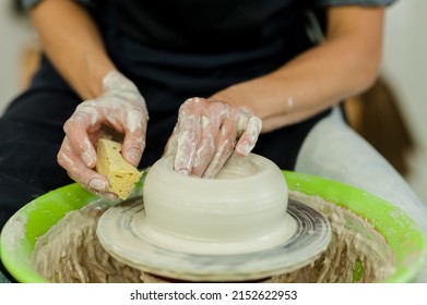master forming jar from wet clay piece in pottery. Unrecognized clay artist modeling product on potters wheel in workshop. Closeup Woman hands sculpting in studio.