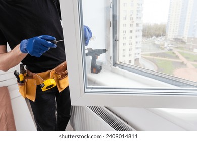 Maestra en guantes ajustando las ventanas de pvc con el destornillador cerrado. Instalación del concepto de reparación y mantenimiento de ventanas de plástico