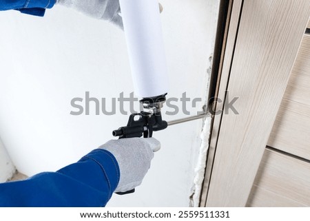 a master in gloves seals a gap between a wall and a door frame with mounting foam