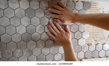 The master glues a mosaic of ceramic tiles. The worker presses the tile with his hands while gluing the tile. The working tiler mounts the tile on the wall, presses it with his hands.